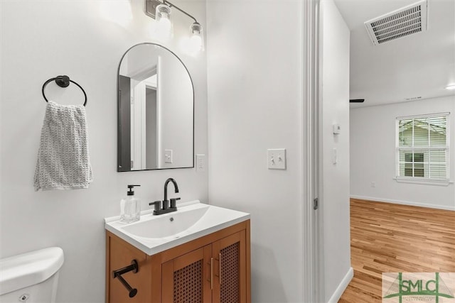 half bathroom featuring toilet, vanity, wood finished floors, and baseboards