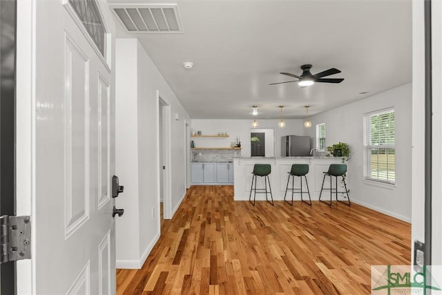 kitchen with freestanding refrigerator, a kitchen bar, light wood finished floors, light countertops, and ceiling fan