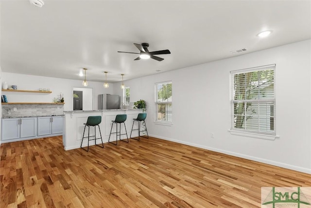 kitchen featuring freestanding refrigerator, a kitchen breakfast bar, light wood-style floors, a ceiling fan, and open shelves
