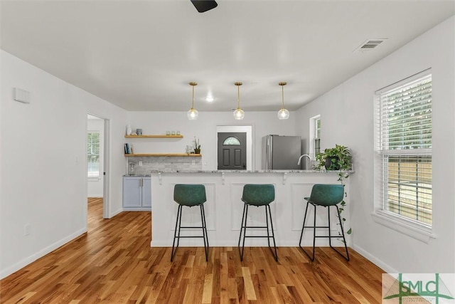 kitchen with freestanding refrigerator, open shelves, a kitchen breakfast bar, a peninsula, and healthy amount of natural light