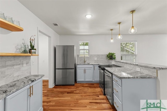 kitchen with appliances with stainless steel finishes, open shelves, a sink, light wood-type flooring, and light stone counters