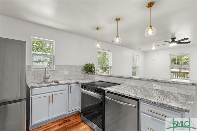 kitchen featuring stainless steel appliances, a sink, a peninsula, light wood-type flooring, and light stone counters
