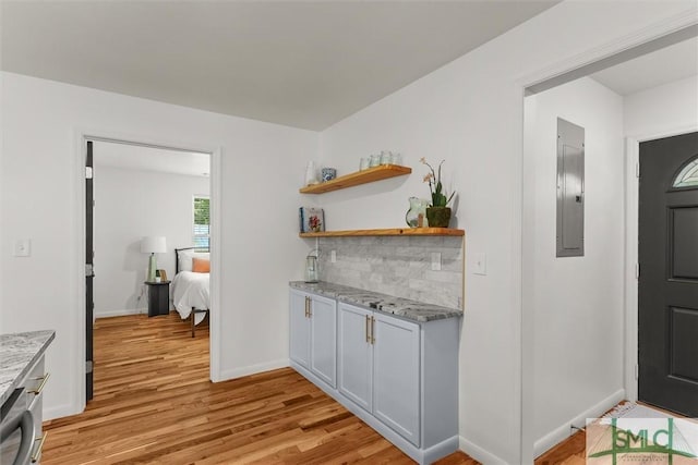 bar featuring light wood-style flooring, baseboards, electric panel, and decorative backsplash