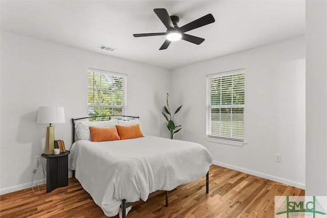 bedroom with multiple windows, wood finished floors, baseboards, and a ceiling fan