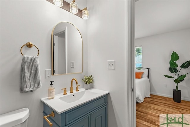 ensuite bathroom featuring toilet, wood finished floors, vanity, and baseboards
