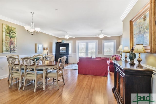 dining room featuring a wainscoted wall, light wood-type flooring, ornamental molding, ceiling fan, and a chandelier