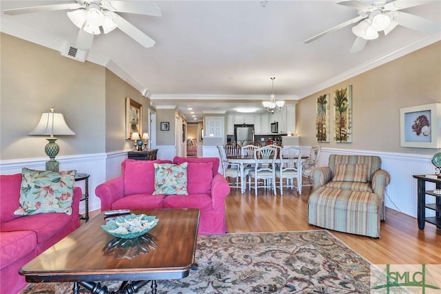 living room featuring ceiling fan, wainscoting, light wood finished floors, and crown molding