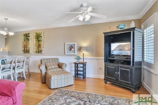living room featuring wood finished floors, crown molding, a ceiling fan, a chandelier, and wainscoting