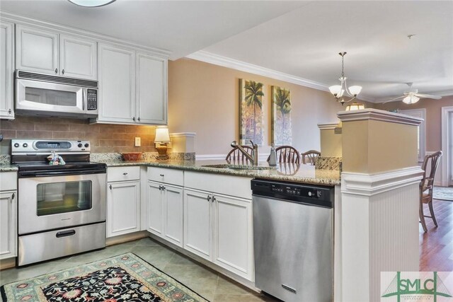 kitchen featuring stainless steel appliances, a sink, backsplash, a peninsula, and white cabinets