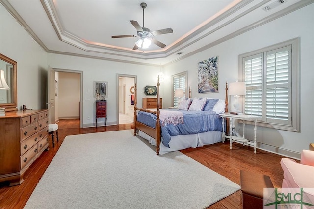 bedroom featuring ornamental molding, wood finished floors, a tray ceiling, baseboards, and ceiling fan