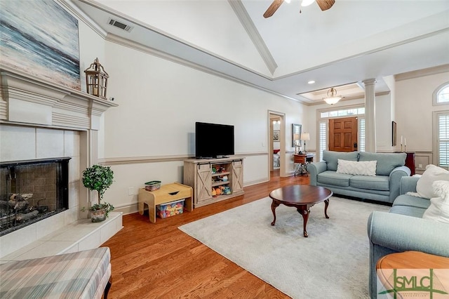 living area with wood finished floors, a tiled fireplace, a ceiling fan, ornamental molding, and baseboards