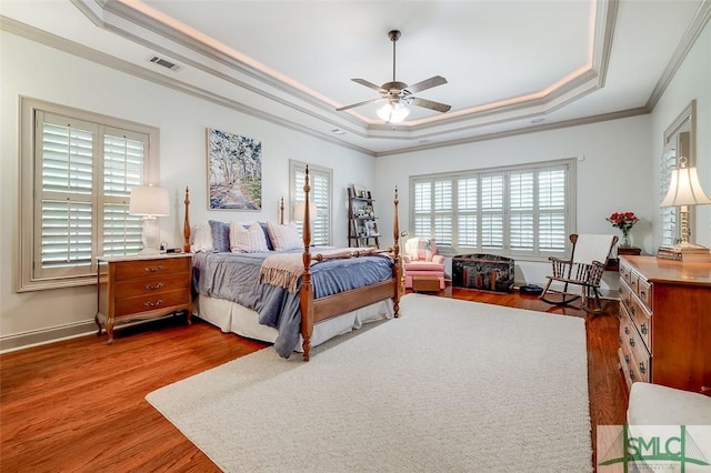 bedroom with a raised ceiling, multiple windows, wood finished floors, ornamental molding, and baseboards