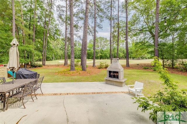view of patio / terrace with exterior fireplace, view of wooded area, and outdoor dining space