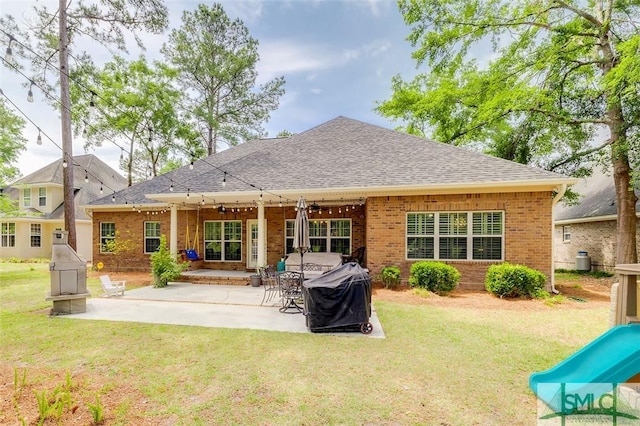 back of property with brick siding, a patio, a yard, and roof with shingles