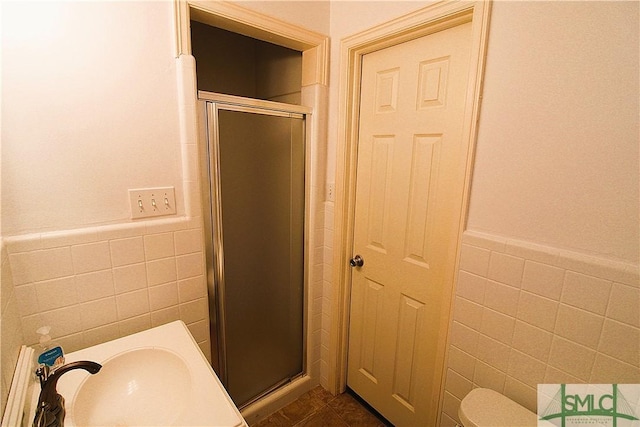 full bathroom with tile walls, a stall shower, a sink, and wainscoting
