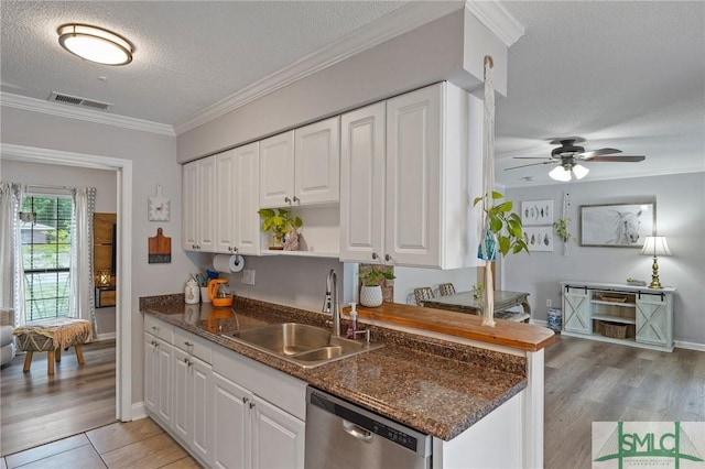 kitchen featuring stainless steel dishwasher, a sink, a textured ceiling, white cabinets, and ornamental molding