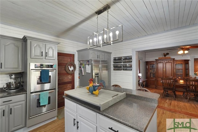 309 E 5th St, Rincon, GA 31326 - kitchen featuring stainless steel appliances, dark countertops, wood walls, light wood finished floors, and gray cabinets