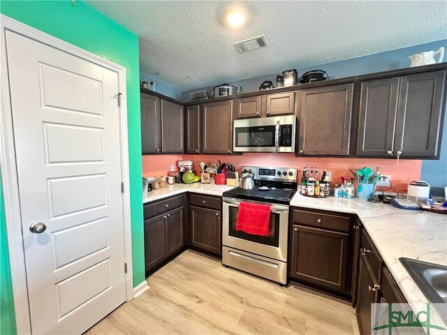 111 Auburn Cir, Glennville, GA 30427 - kitchen featuring appliances with stainless steel finishes, dark brown cabinets, light wood-style floors, a textured ceiling, and light stone counters