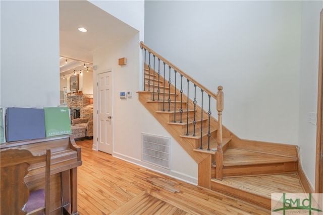 staircase with wood finished floors, baseboards, recessed lighting, and a stone fireplace