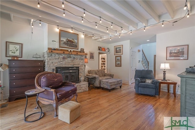living area with light wood-style flooring, a fireplace, stairway, baseboards, and beamed ceiling