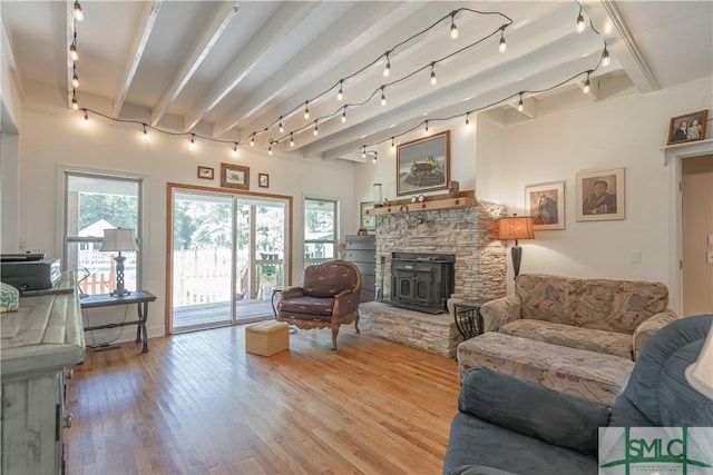 living area with track lighting, wood finished floors, a stone fireplace, and beam ceiling