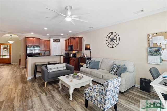 living room with ceiling fan, arched walkways, ornamental molding, light wood-type flooring, and recessed lighting