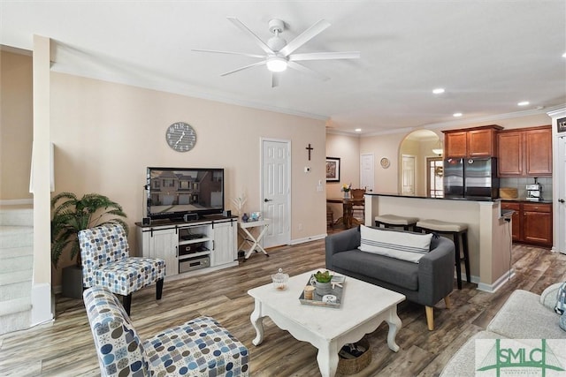 living area featuring arched walkways, a ceiling fan, light wood-style floors, recessed lighting, and ornamental molding