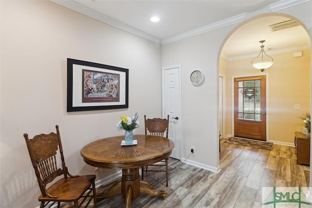 dining space with arched walkways, light wood finished floors, crown molding, baseboards, and recessed lighting