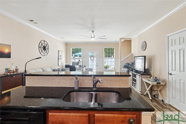 kitchen with open floor plan, a sink, ornamental molding, dark stone counters, and a kitchen island with sink