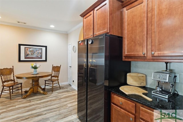 kitchen with ornamental molding, freestanding refrigerator, light wood-style flooring, dark stone counters, and tasteful backsplash