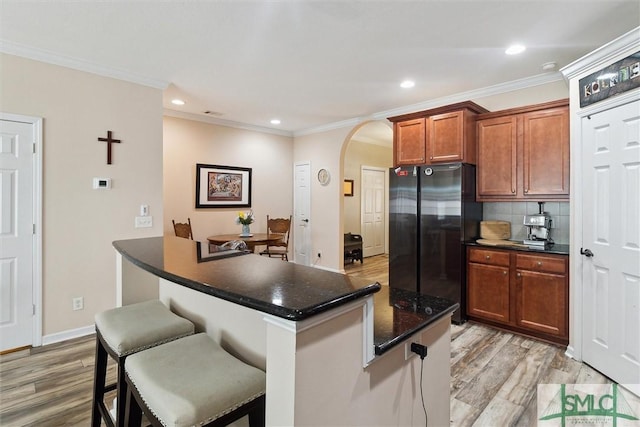 kitchen with freestanding refrigerator, arched walkways, light wood-style floors, a breakfast bar area, and decorative backsplash