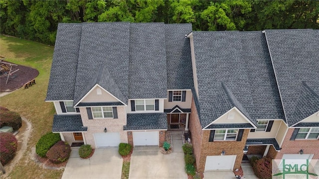 view of front of property with concrete driveway, roof with shingles, brick siding, a garage, and a front yard