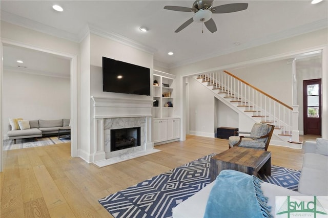 living area featuring stairs, a ceiling fan, wood finished floors, ornamental molding, and a premium fireplace
