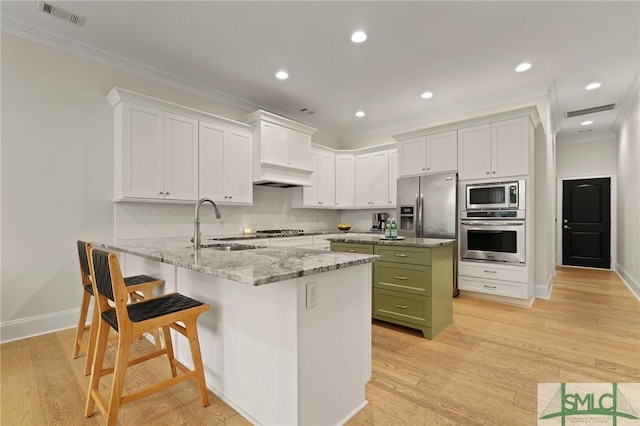 kitchen with stainless steel appliances, green cabinets, ornamental molding, a sink, and a peninsula