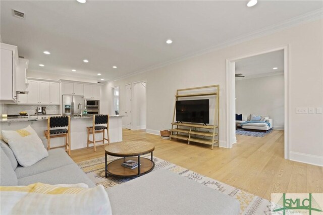 living room with light wood-style floors, ornamental molding, recessed lighting, and baseboards