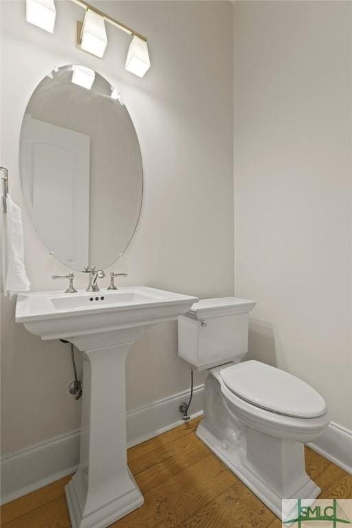 half bath with toilet, wood finished floors, and baseboards