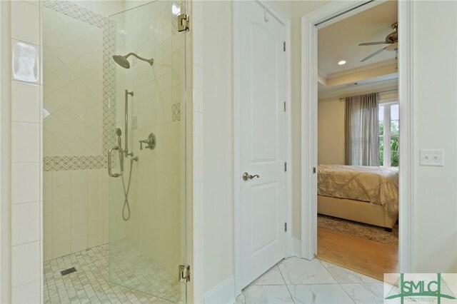 ensuite bathroom featuring a stall shower, marble finish floors, a ceiling fan, crown molding, and a tray ceiling