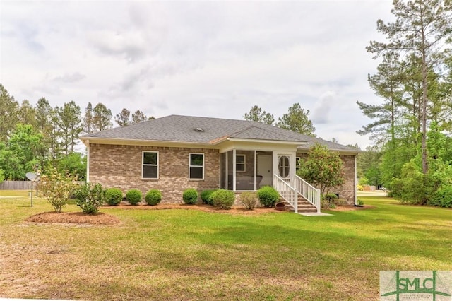 view of front of home with a sunroom, a front yard, brick siding, and a shingled roof