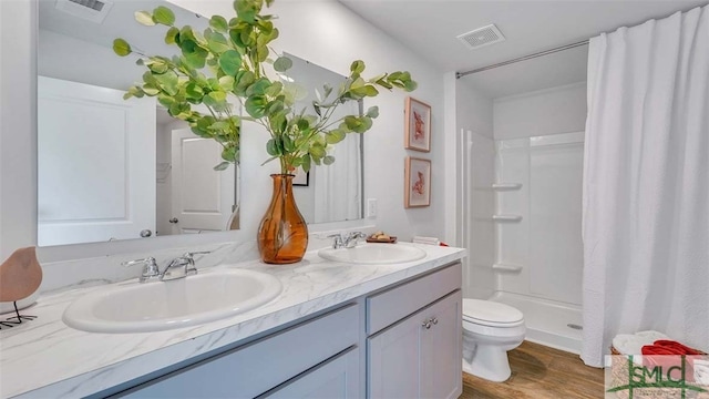 bathroom with toilet, a shower stall, wood finished floors, and double vanity