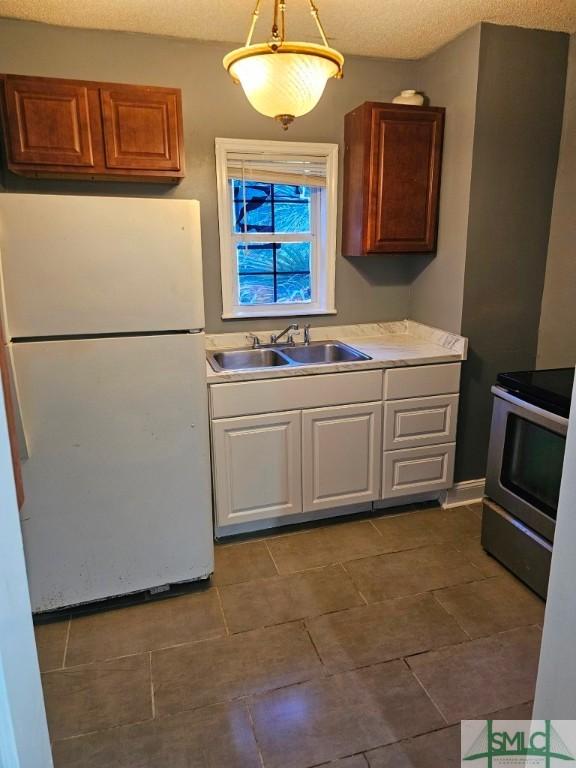kitchen with freestanding refrigerator, a sink, stainless steel electric range, light countertops, and white cabinets