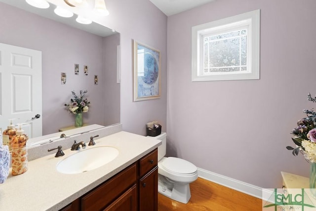 half bathroom with toilet, wood finished floors, vanity, and baseboards