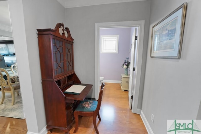 hallway with light wood finished floors, baseboards, and crown molding