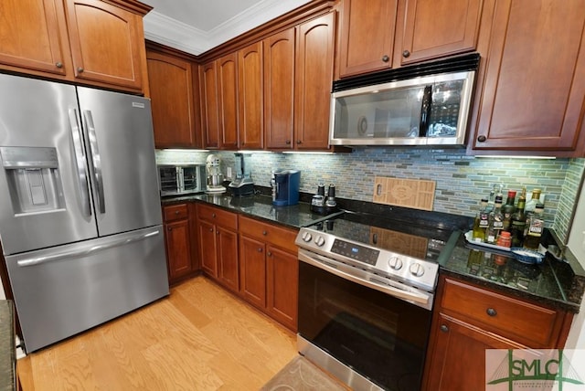 kitchen with appliances with stainless steel finishes, light wood-style flooring, dark stone countertops, crown molding, and backsplash