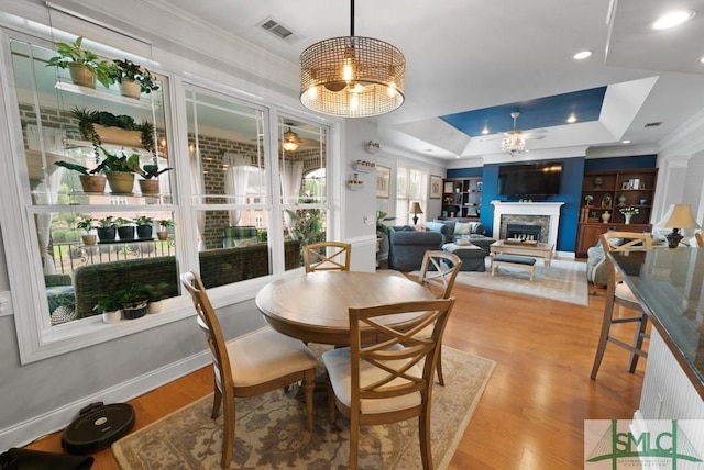 dining space featuring a raised ceiling, a ceiling fan, crown molding, a fireplace, and wood finished floors
