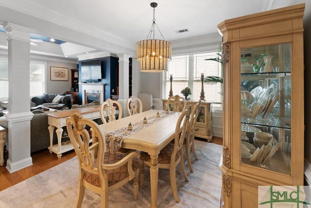 dining area with ornate columns, healthy amount of natural light, crown molding, light wood-type flooring, and a chandelier