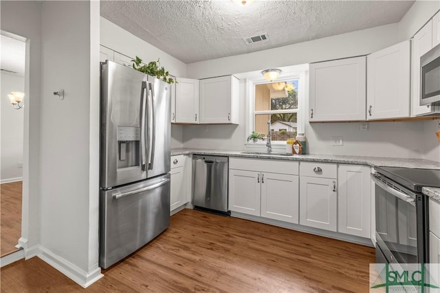 108 Gilliam Ave, Savannah, GA 31406 - kitchen featuring stainless steel appliances, a sink, white cabinets, wood finished floors, and a textured ceiling