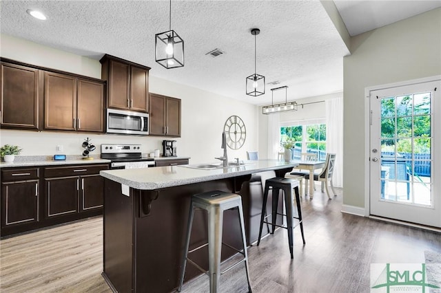 kitchen featuring stainless steel appliances, a sink, light wood-style floors, a kitchen breakfast bar, and light countertops