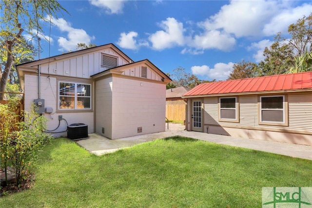back of property with central AC unit, board and batten siding, metal roof, and a patio