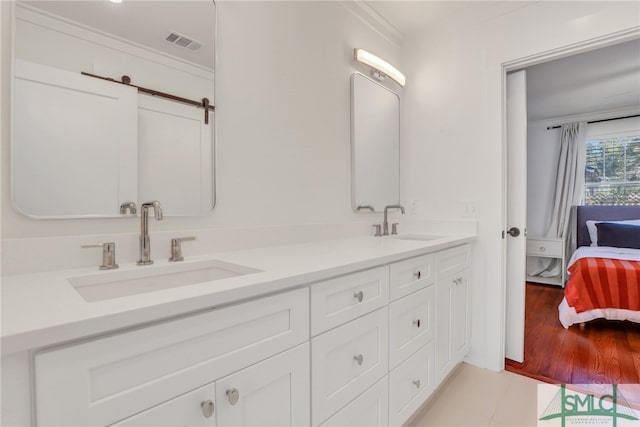 ensuite bathroom with double vanity, ornamental molding, and wood finished floors