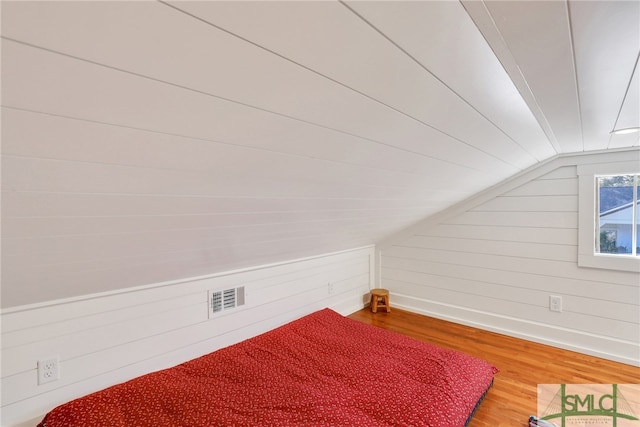 bedroom featuring wood finished floors, lofted ceiling, wooden walls, and baseboards